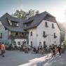 Ein traditionelles Gasthaus mit Menschen im Freien bei Sonnenschein.