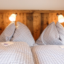 A cozy double bed with checkered duvet covers and two reading lamps mounted on a wooden headboard.