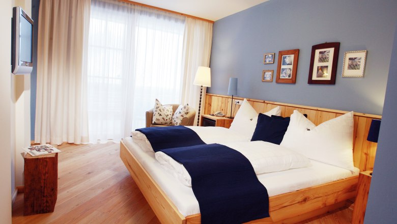Gemütliches Hotelzimmer mit Doppelbett, blauen Akzenten und Holzmöbeln.