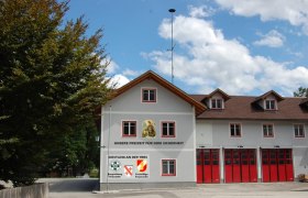 Feuerwehrgeb&auml;ude mit roten Toren und Schriftzug 'Unsere Freizeit f&uuml;r Ihre Sicherheit'.