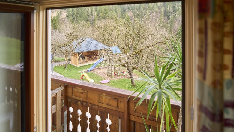 Blick aus einem Fenster auf einen Garten mit Spielplatz und Holzh&uuml;tte.