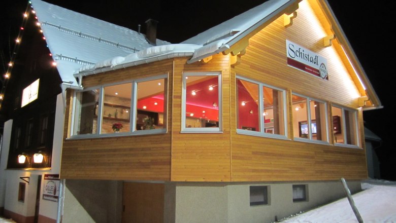 An illuminated building in the snow with the sign 'Schistadl'.