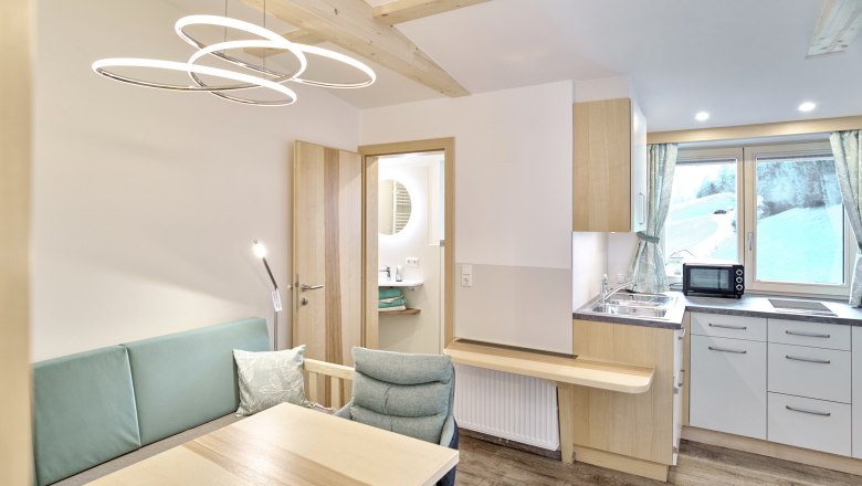 Modernes Apartment mit Holzm&ouml;beln, kleiner K&uuml;che und Blick aus dem Fenster auf eine verschneite Landschaft.