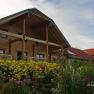 A traditional farmhouse with wooden cladding and a flowering garden in the foreground.