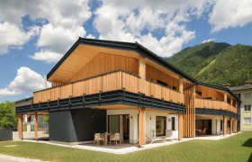 A modern wooden building with a balcony and a mountain backdrop.