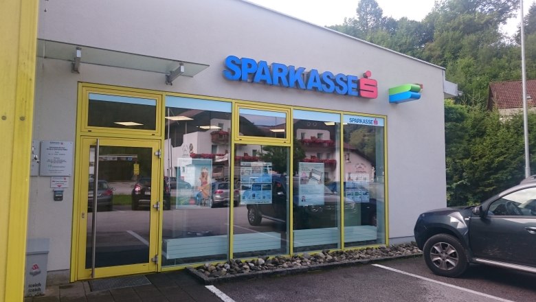 Eingang einer Sparkasse-Filiale mit gelbem Rahmen und Glastüren.