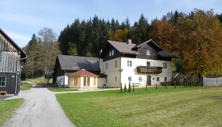 Ein gro&szlig;es, zweist&ouml;ckiges Haus mit Balkon, umgeben von Wiesen und B&auml;umen im Herbst.