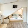 Kompaktes Apartment mit eingebautem Bett unter einer Dachschr&auml;ge, K&uuml;chenzeile und Fernseher.