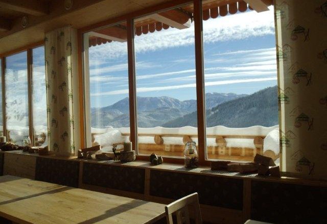 Blick aus einem Fenster auf verschneite Berge und blauen Himmel.