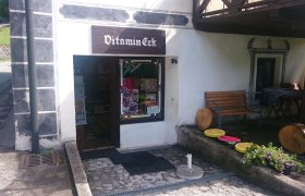 Eingang eines kleinen Ladens namens Vitamin-Eck mit Sitzbank und Dekorationen aus Holz und Blumen.