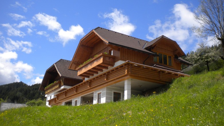 Ein traditionelles Holzhaus auf einem grünen Hügel unter blauem Himmel.