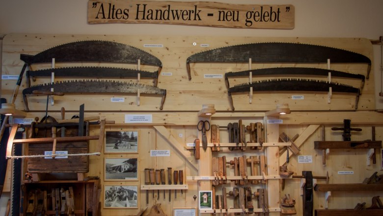 Ausstellung von alten Handwerkzeugen an einer Holzwand mit dem Schild 'Altes Handwerk - neu gelebt'.