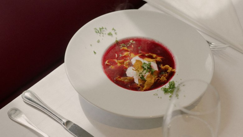 Ein Teller mit roter R&uuml;bensuppe, garniert mit Sahne und Kr&auml;utern, auf einem gedeckten Tisch.