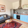 Gem&uuml;tliche K&uuml;che mit blauen Schr&auml;nken, grauem Sofa und buntem Teppich.