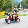 A child is riding a small pedal tractor with a shovel on an outdoor path.