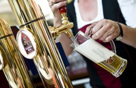 Eine Person zapft Bier aus einem goldenen Zapfhahn in ein Glas mit Schaumkrone.