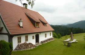 Ein traditionelles Ferienhaus mit rotem Ziegeldach in einer grünen, hügeligen Landschaft.