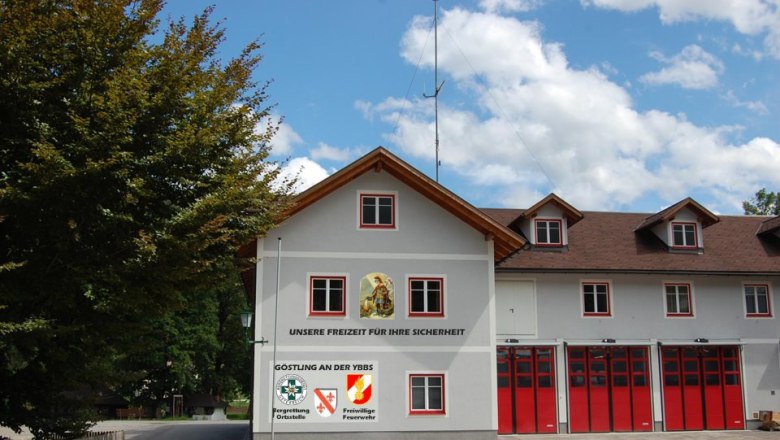 Feuerwehrgeb&auml;ude mit roten Toren und Schriftzug 'Unsere Freizeit f&uuml;r Ihre Sicherheit'.