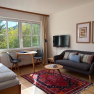 Cozy living room with a sofa, table, chairs, and a large window overlooking the greenery.